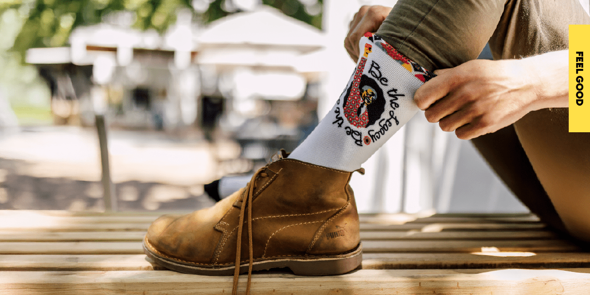 A close-up of a custom sock featuring the Nelson Mandela Day campaign logo being pulled up, worn with a leather shoe to celebrate our community support initiatives.