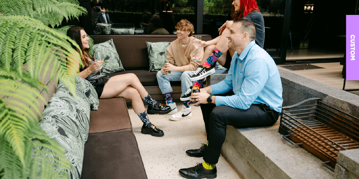A group of co-workers chatting casually while wearing vibrant, mismatched custom socks that symbolise team spirit and unity for their year-end function.